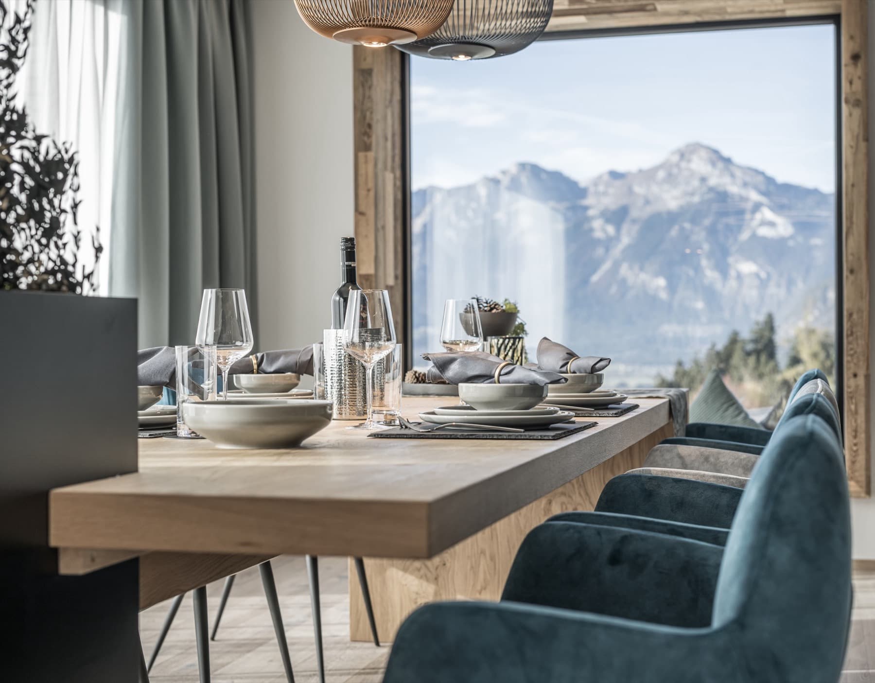 Inviting laid wooden table with blue armchairs and large windows opening onto an impressive mountain panorama.