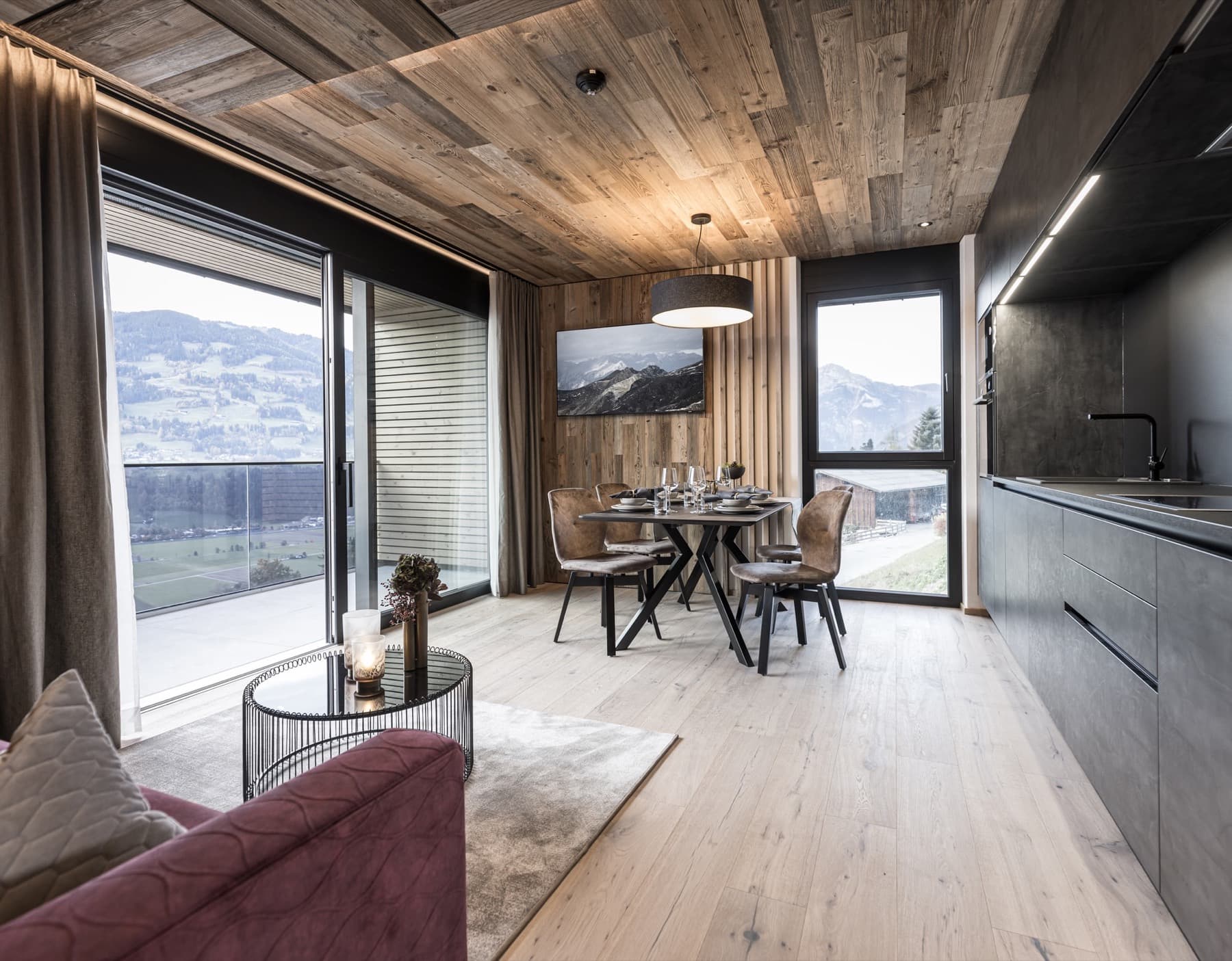 Open living area with a modern kitchen, laid dining table, cosy sofa and large windows with mountain views.