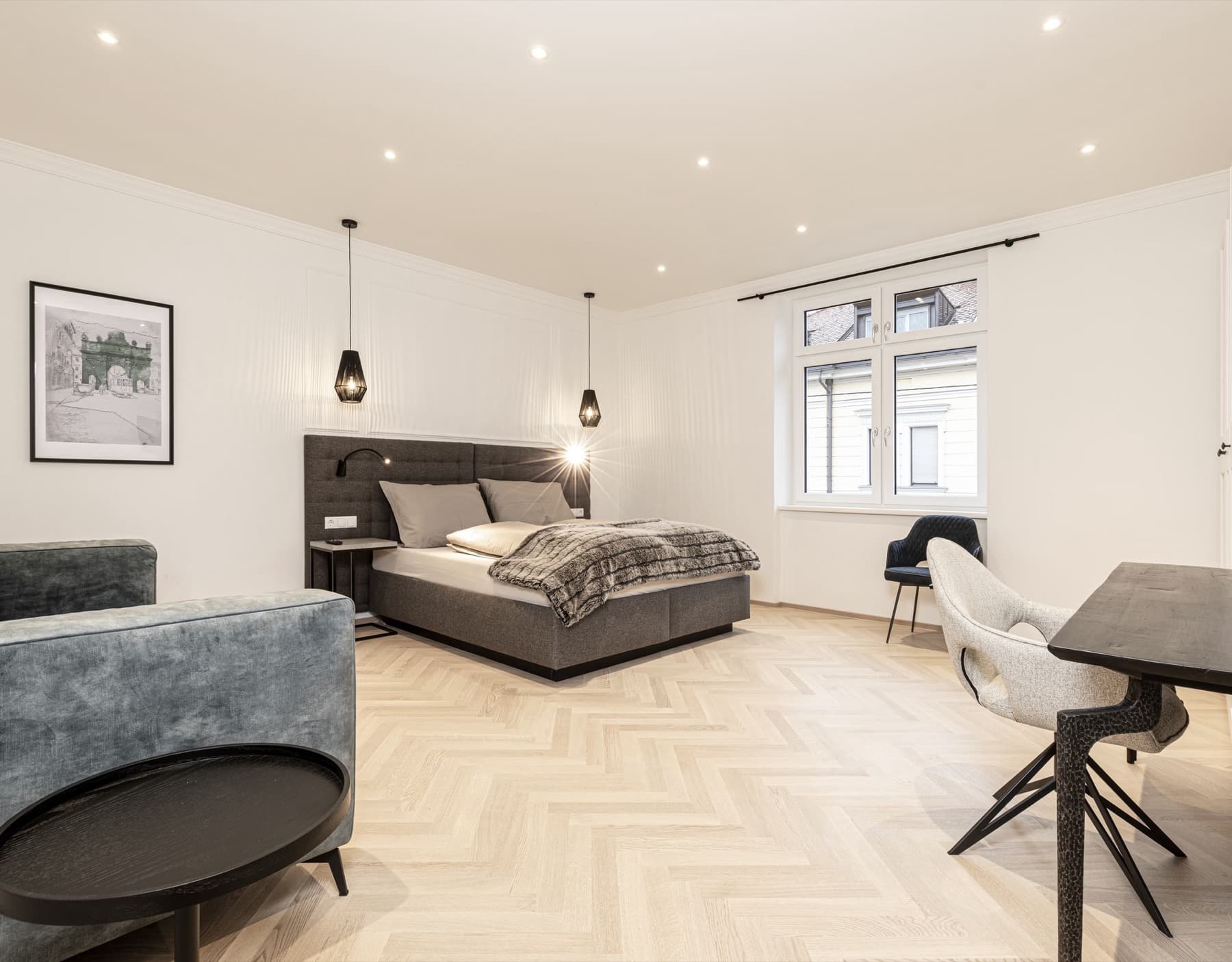 Großzügiges helles Zimmer mit Doppelbett, graugrünem Sofa, Esstisch und mehreren bequemen Polsterstühlen.