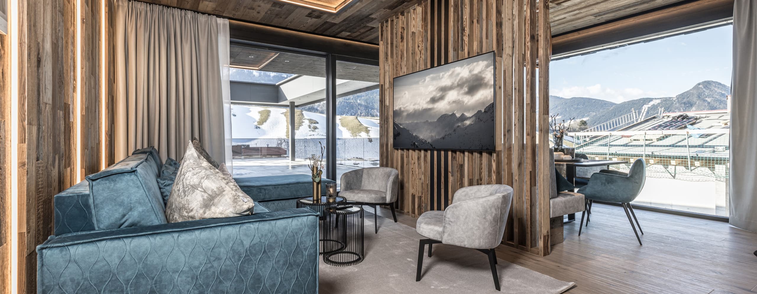 Wohnraum mit blauem Sofa, Altholzwänden und Blick auf die Berge