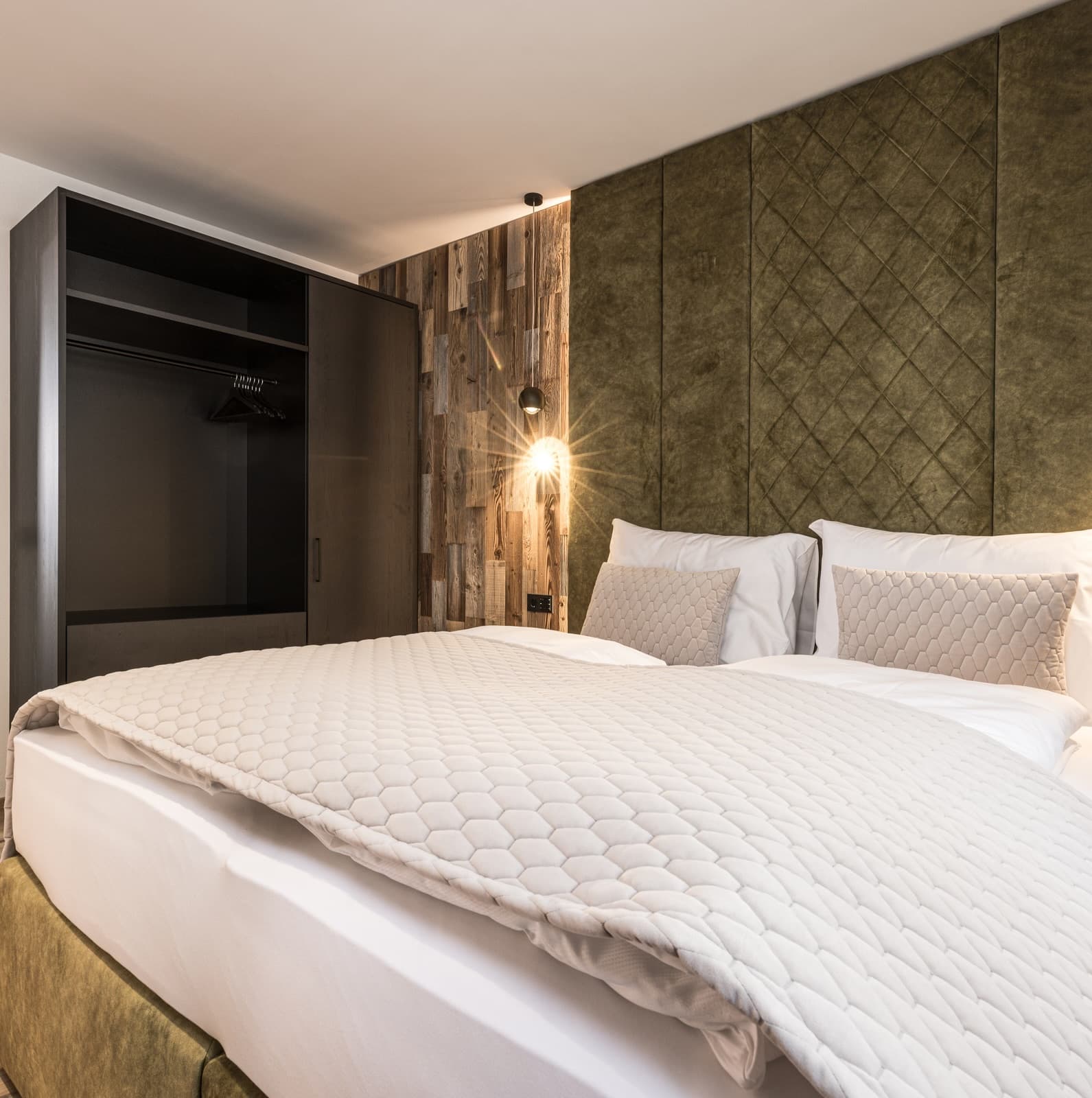 Modernes Schlafzimmer mit großem Doppelbett, grünem gepolstertem Kopfteil, rustikalen Holzelementen und offenem Kleiderschrank.